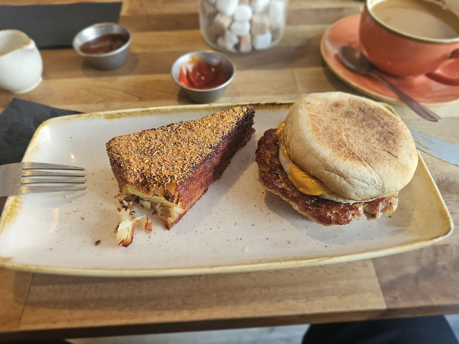 A breakfast muffin with sausage, egg and cheese next to a wedge of seasoned hashbrown at Ethos, Havant